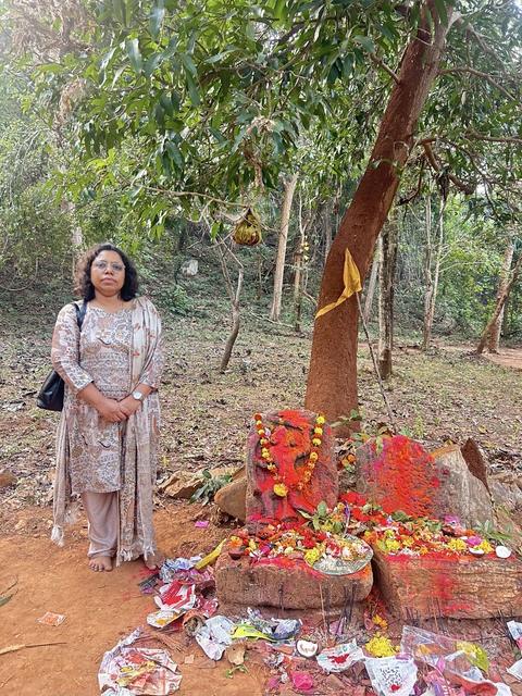 Woman standing beside a forest shrine with offerings