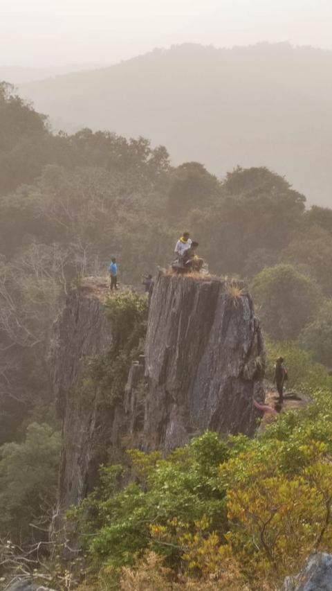 People on a rocky cliff above forested hills