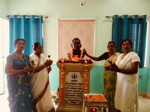Four women offering roses at the garlanded memorial bust