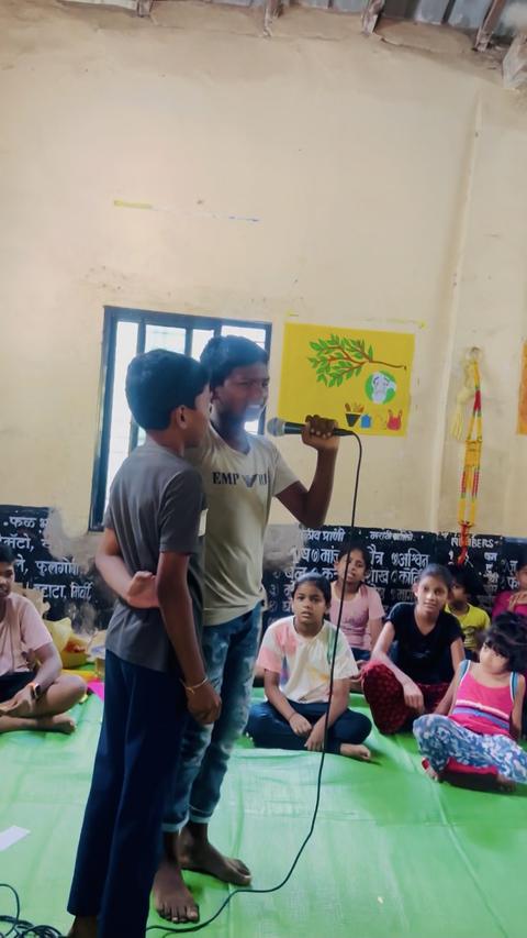 Two boys speaking into a microphone before seated children